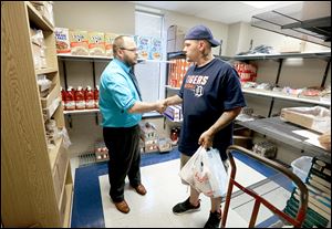 Sam Adams, a community health worker at the Mercy Health Franklin Avenue Medical Center, left, shakes hands with client Joshua Ropp, after assisting and then providing him with goods from the food bank.