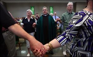 Fr. Herb Weber, Pastor, holds hands and prays during Sunday mass at St. John XXIII in Perrysburg on July 2, 2017.