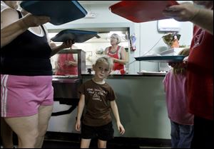 Kimberly Slover is framed by trays of food carried by Debra Born, left, and Roger Steinman, right, at the Helping Hands of St. Louis Outreach Center in East Toledo in 2012. The facility, which has a food pantry, soup kitchen, and clothing center, is celebrating its 30th anniversary. 