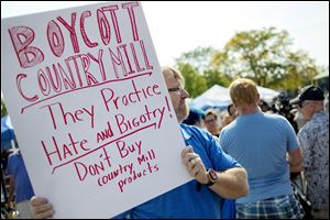 Lansing, Mich., resident Kennan DeWitt holds up a sign near the Country Mill booth in protest on Sunday, Sept. 17, 2017, at the East Lansing Farmer's Market.