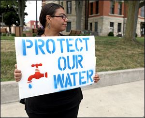 Norah Gonzalez, of Bryan, Ohio, holds up a sign for passing cars and pedestrians to see during a protest next to the Williams County Courthouse in Bryan, Ohio, on Sunday, July 29, 2018. Toledo-area susburbs are exploring using the Michindoh Aquifer as a water source.