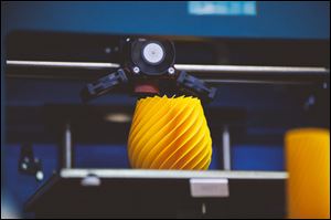 A blue 3D printer creates a yellow plastic object.