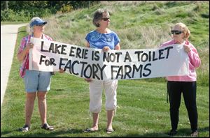 From left Diane Stein, Kathy Mockensturm, and Nancy Roffey of Advocates for a Clean Lake Erie hold up a sign Wednesday at Middlegrounds Metropark in Toledo.